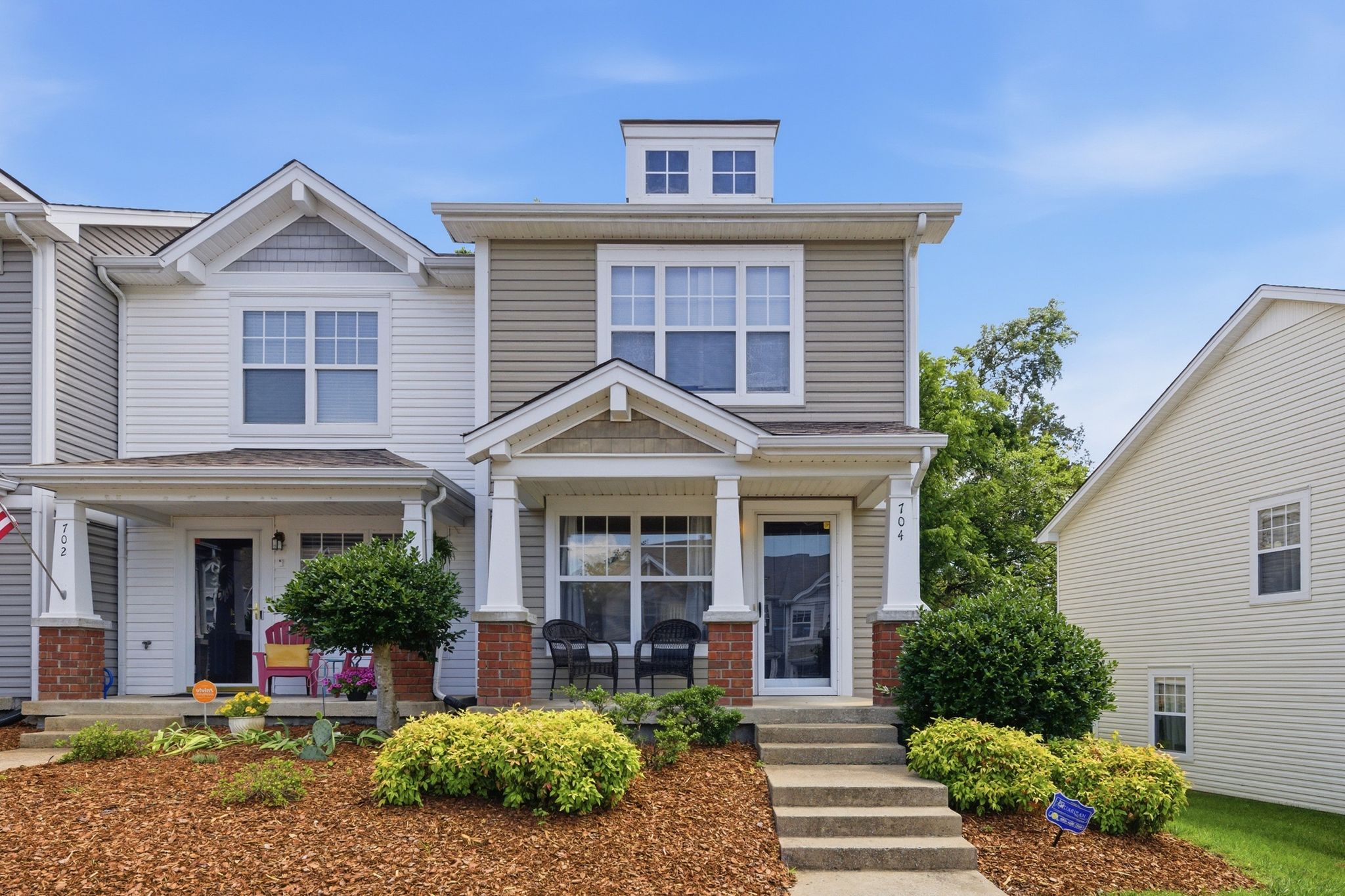 Two-story suburban house with beige siding, white trim, and a small front porch with chairs.
