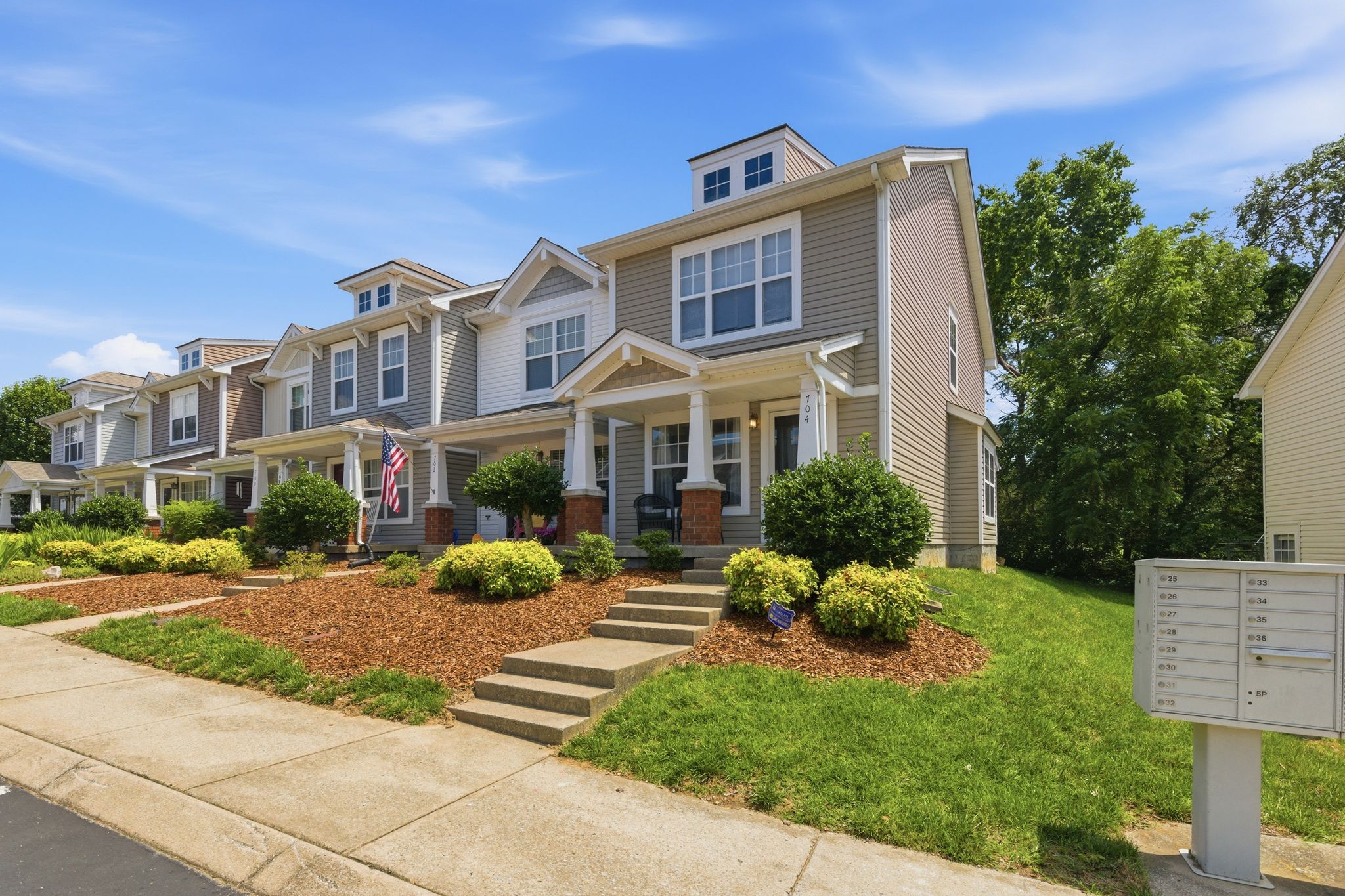 Row of beige two-story townhouses with porches and well-kept landscaping under a blue sky. (informative)