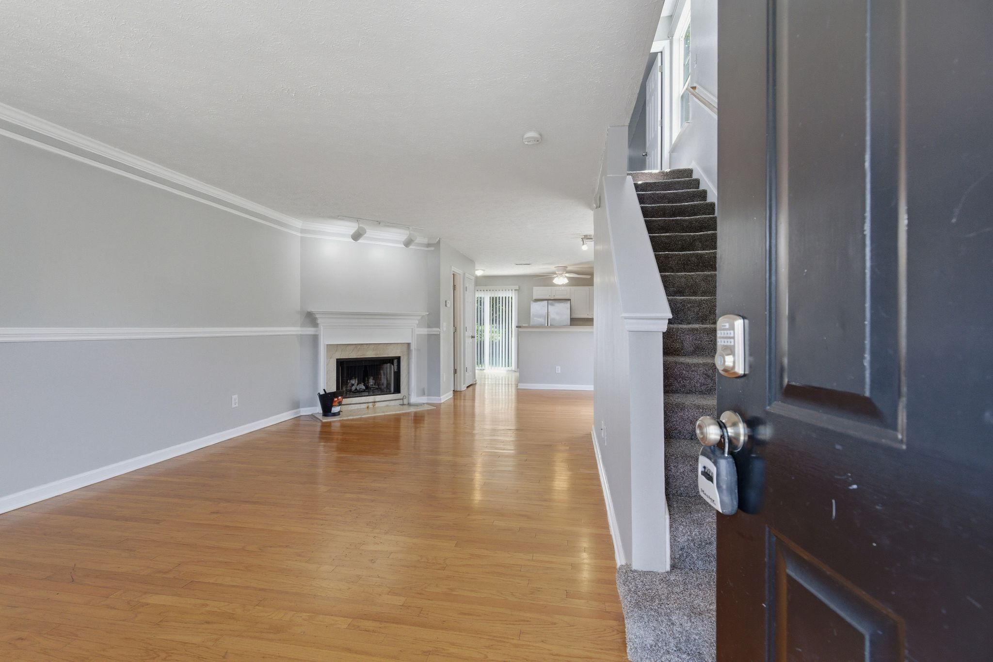 Open living room with hardwood floors, fireplace on the left, and a carpeted staircase on the right leading upstairs, viewed from the entryway door.