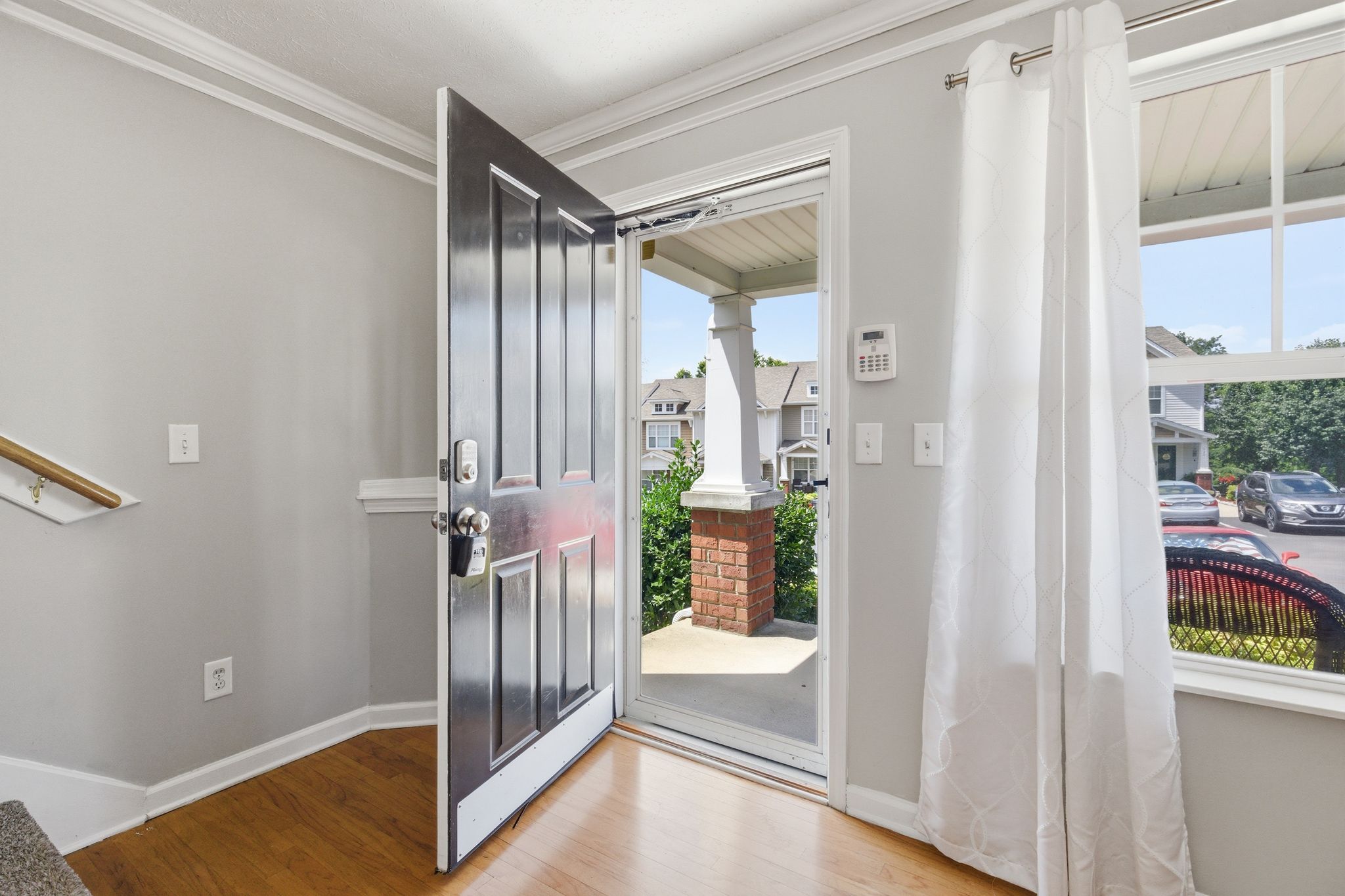 Open front door into a bright entryway with a view of the porch and neighborhood outside, including a brick post.