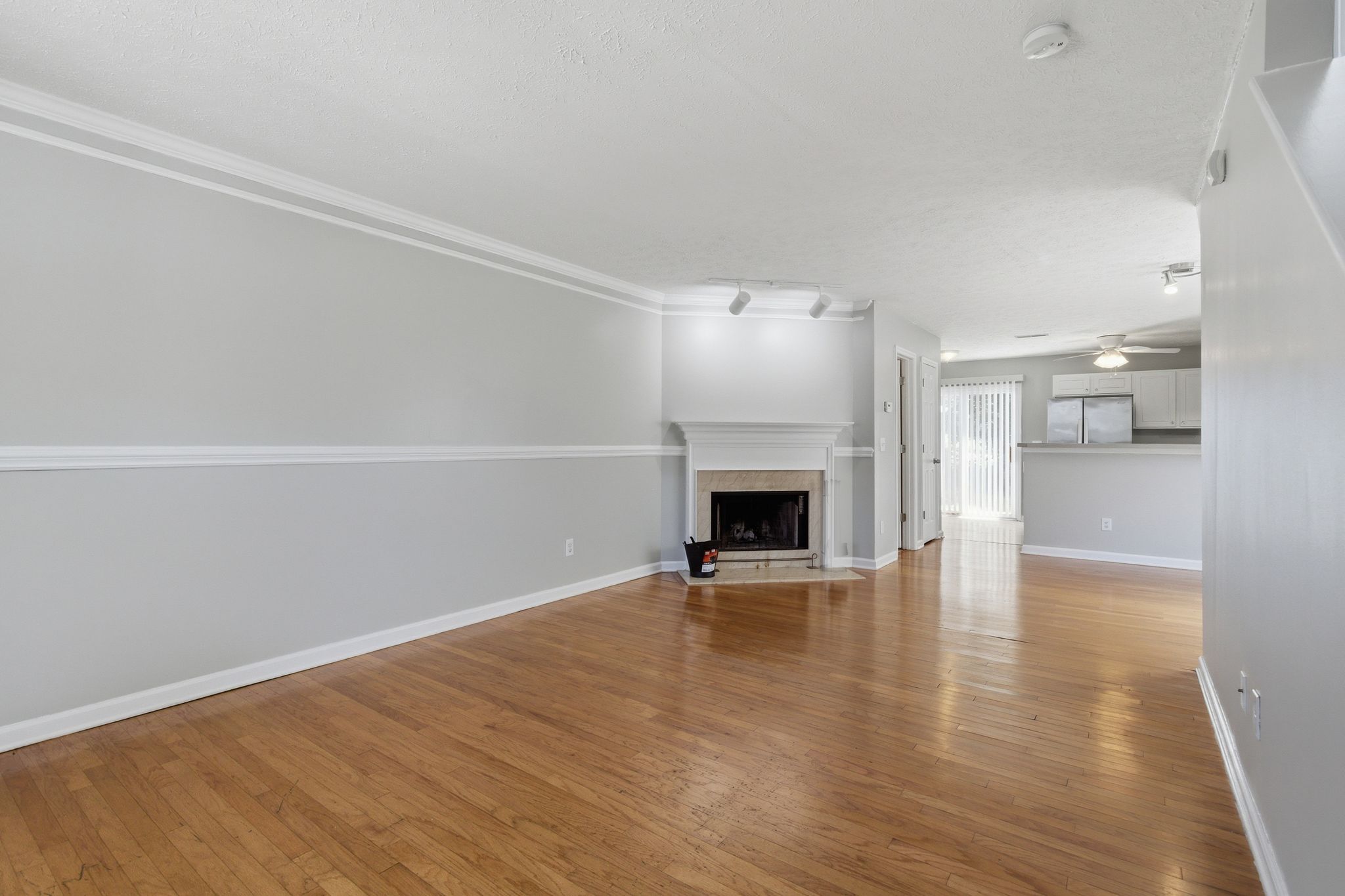 Spacious living room with gray walls, white trim, and a fireplace; kitchen visible in the background.