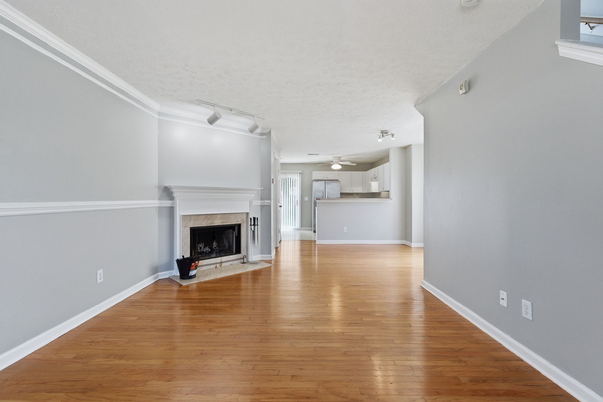 Spacious living room with gray walls, white trim and hardwood floors, fireplace on the left and an open kitchen in the background.