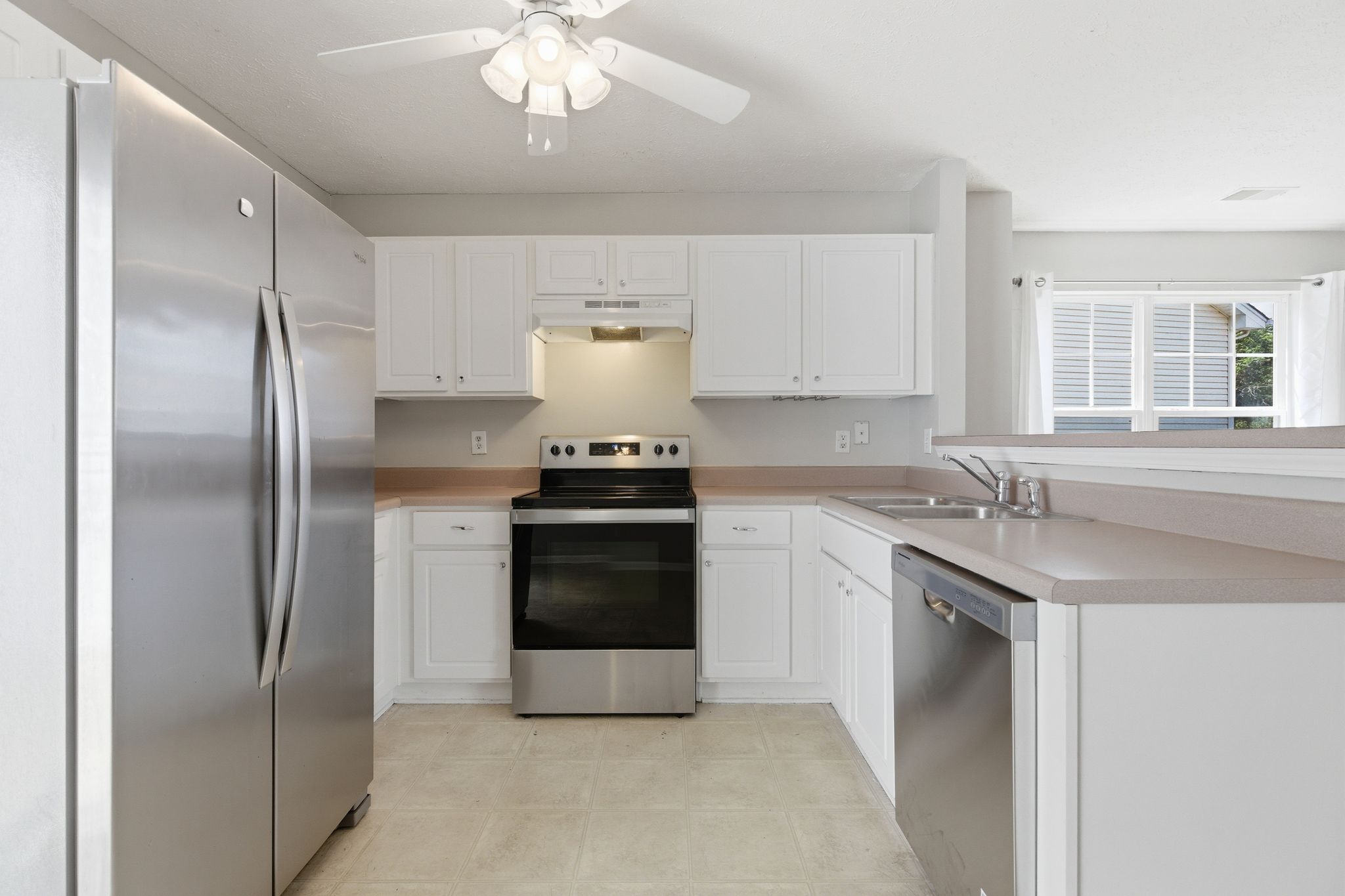 Modern white kitchen with stainless steel appliances, white cabinetry, and a window over the sink.