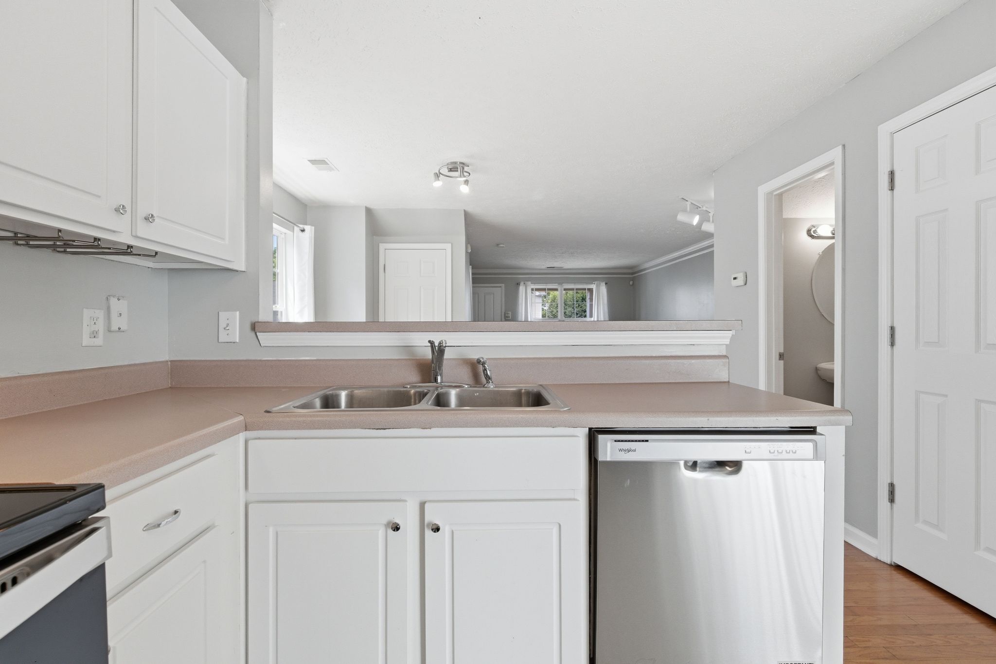 White kitchen with beige countertops, double sink, and a stainless dishwasher under a pass-through counter.