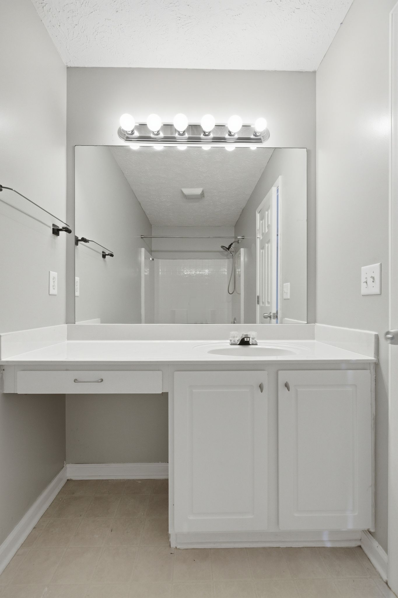 White bathroom vanity with two cabinet doors, large mirror, and a six-bulb light bar above the sink area.