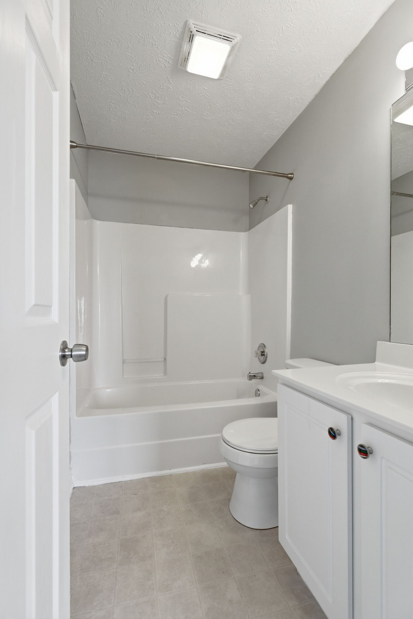 Small white bathroom with tub/shower, shower rod, toilet, and vanity seen from doorway