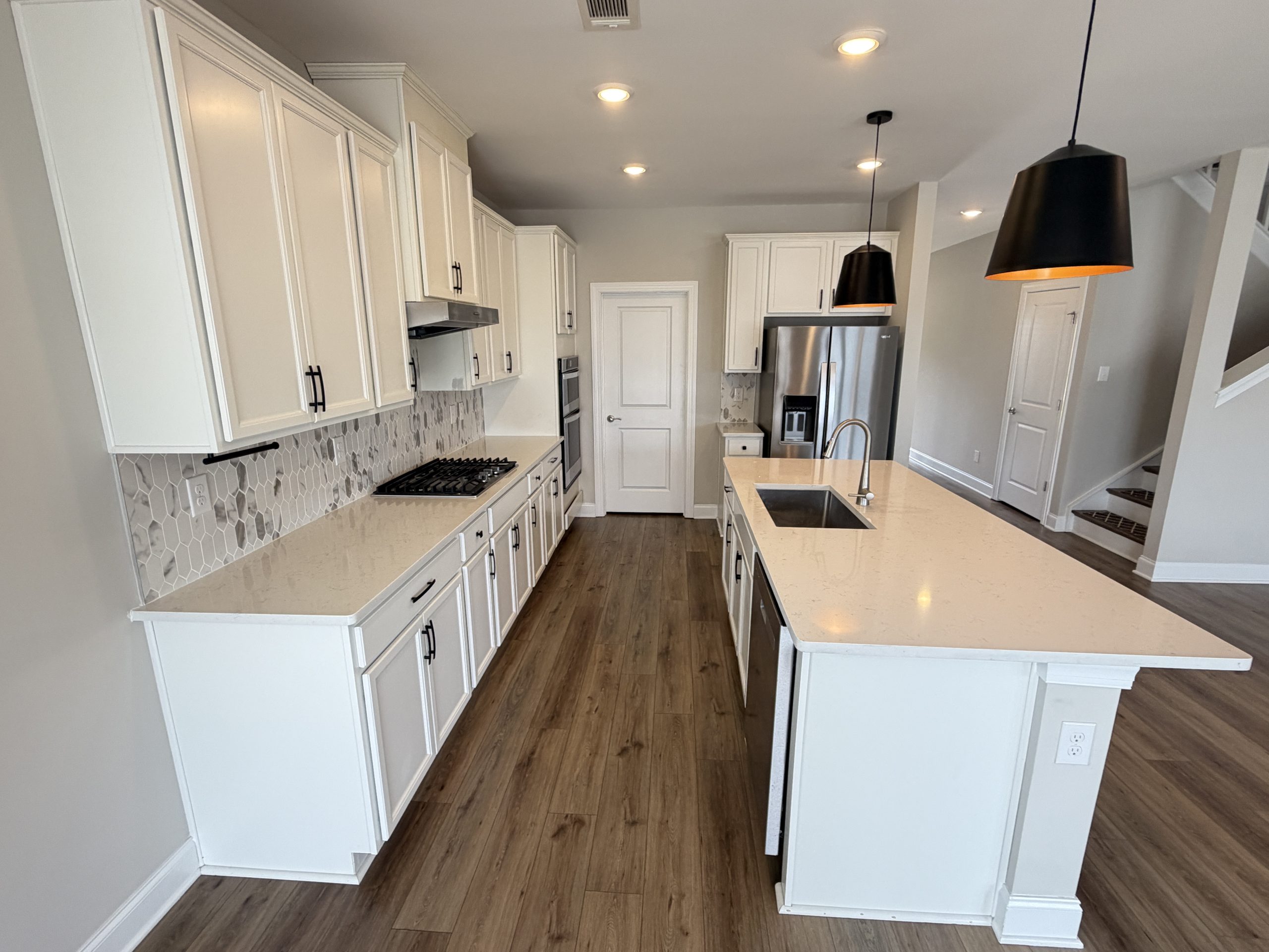 Bright modern kitchen with white cabinetry, stone countertops, hex tile backsplash, stainless appliances, and black pendant lights over an island sink.