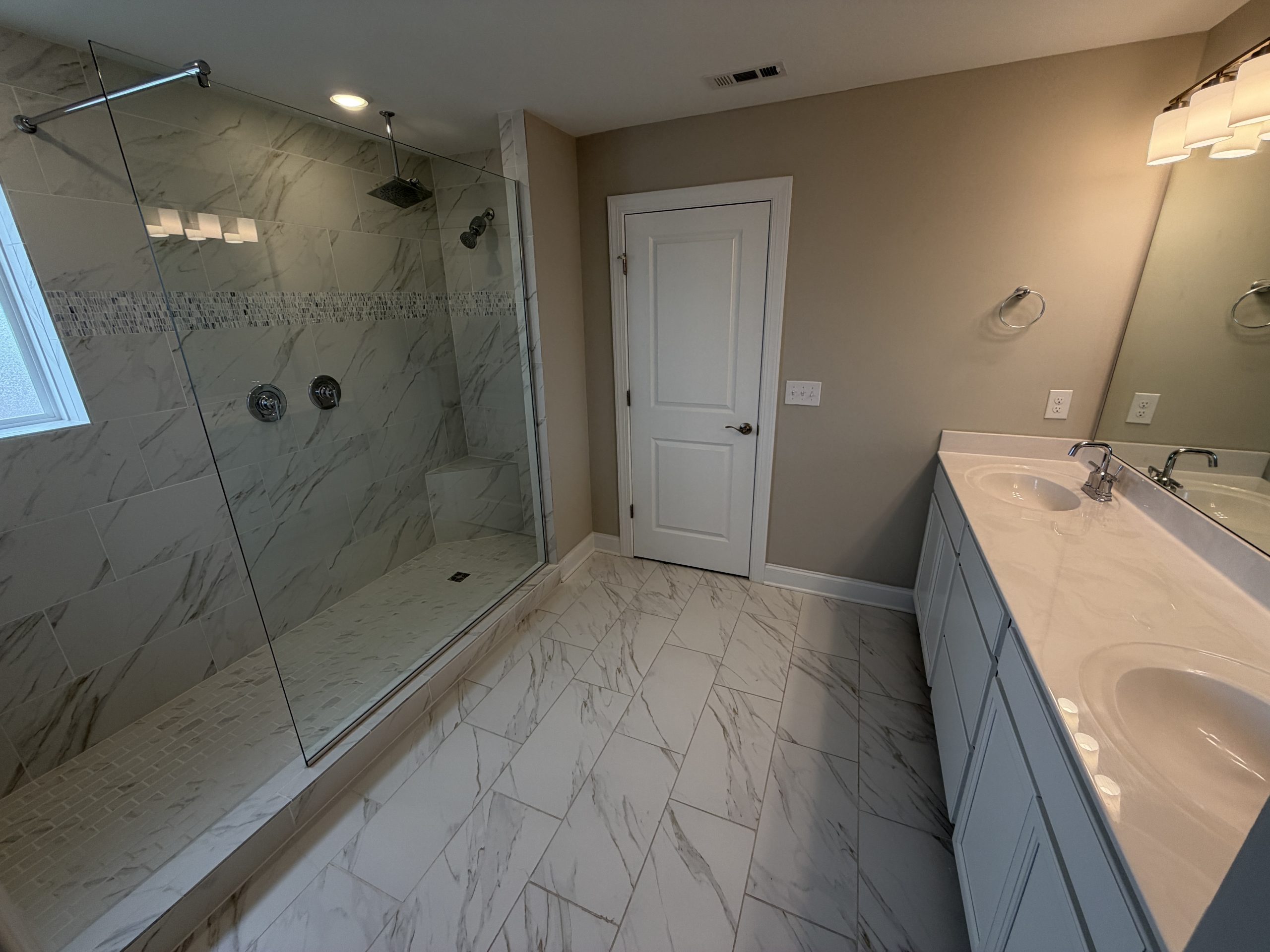 Modern bathroom with glass shower enclosure, marble tile walls and floor, and a white double-sink vanity.