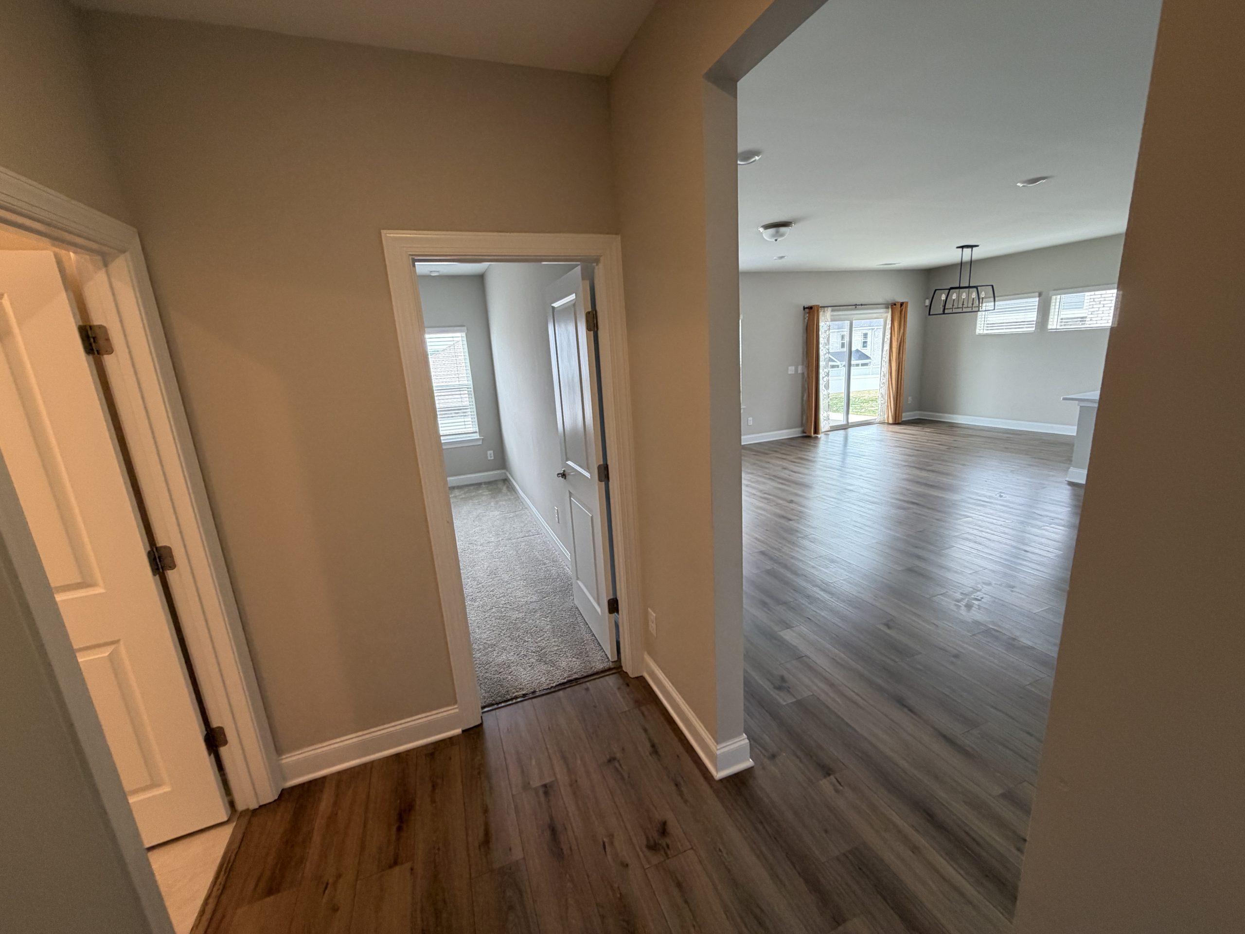 Hallway opening into a bright open-concept living area with wood floors, large windows, and a hanging light fixture.