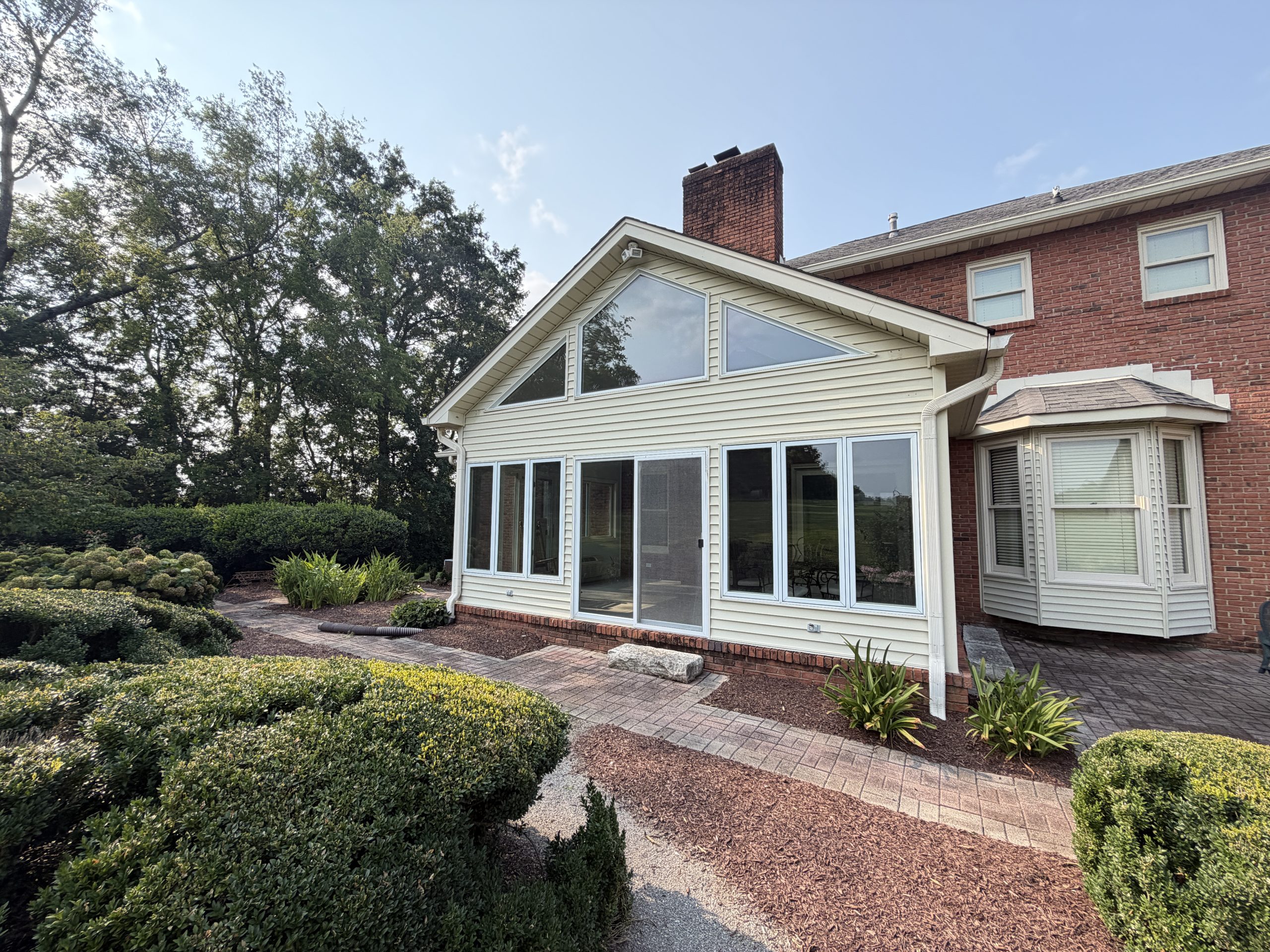 Brick house with a large glass-walled sunroom and manicured garden path in the foreground.
