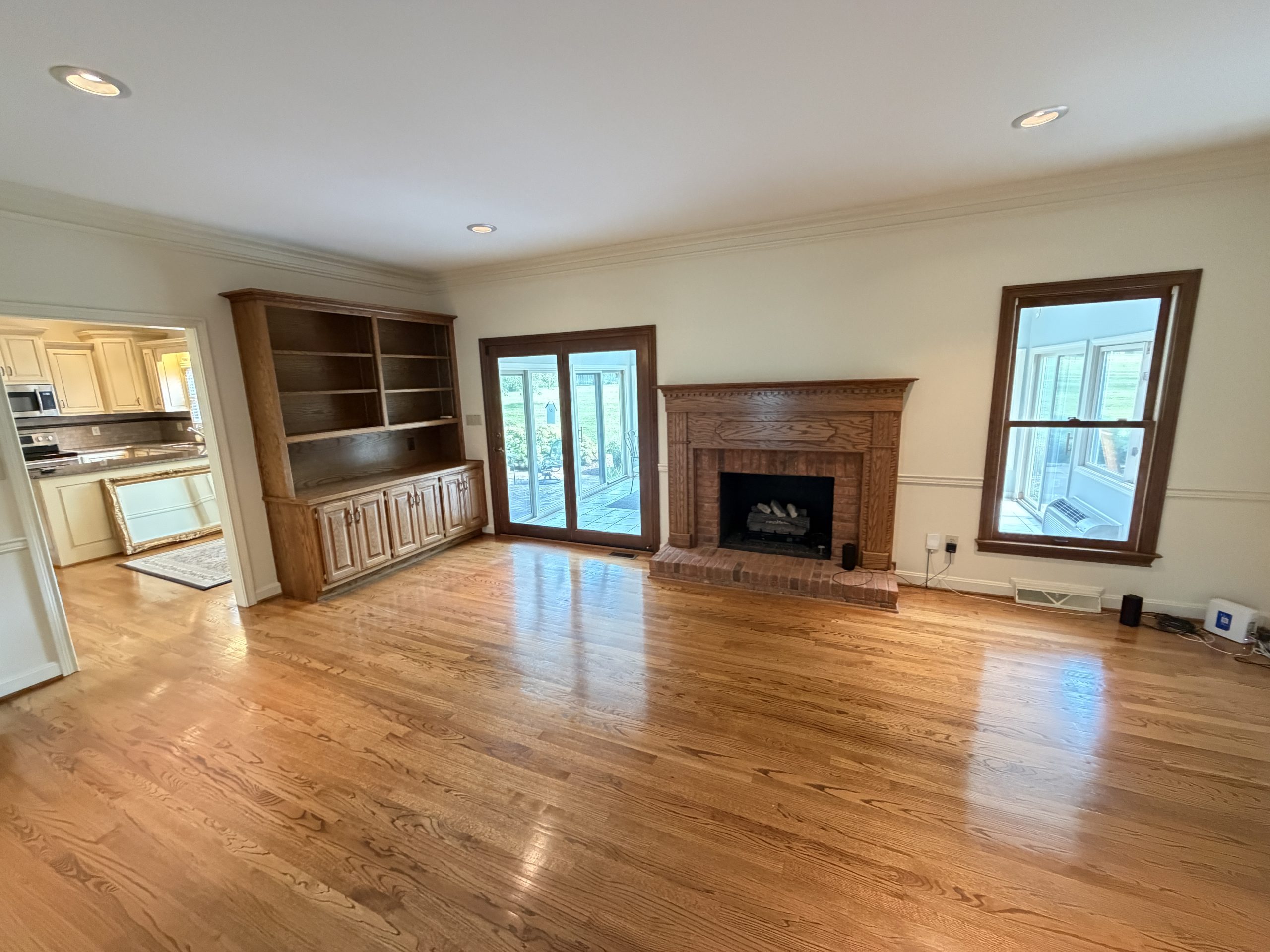 Living room with hardwood floors, built-in wooden cabinets, brick fireplace, and large windows.