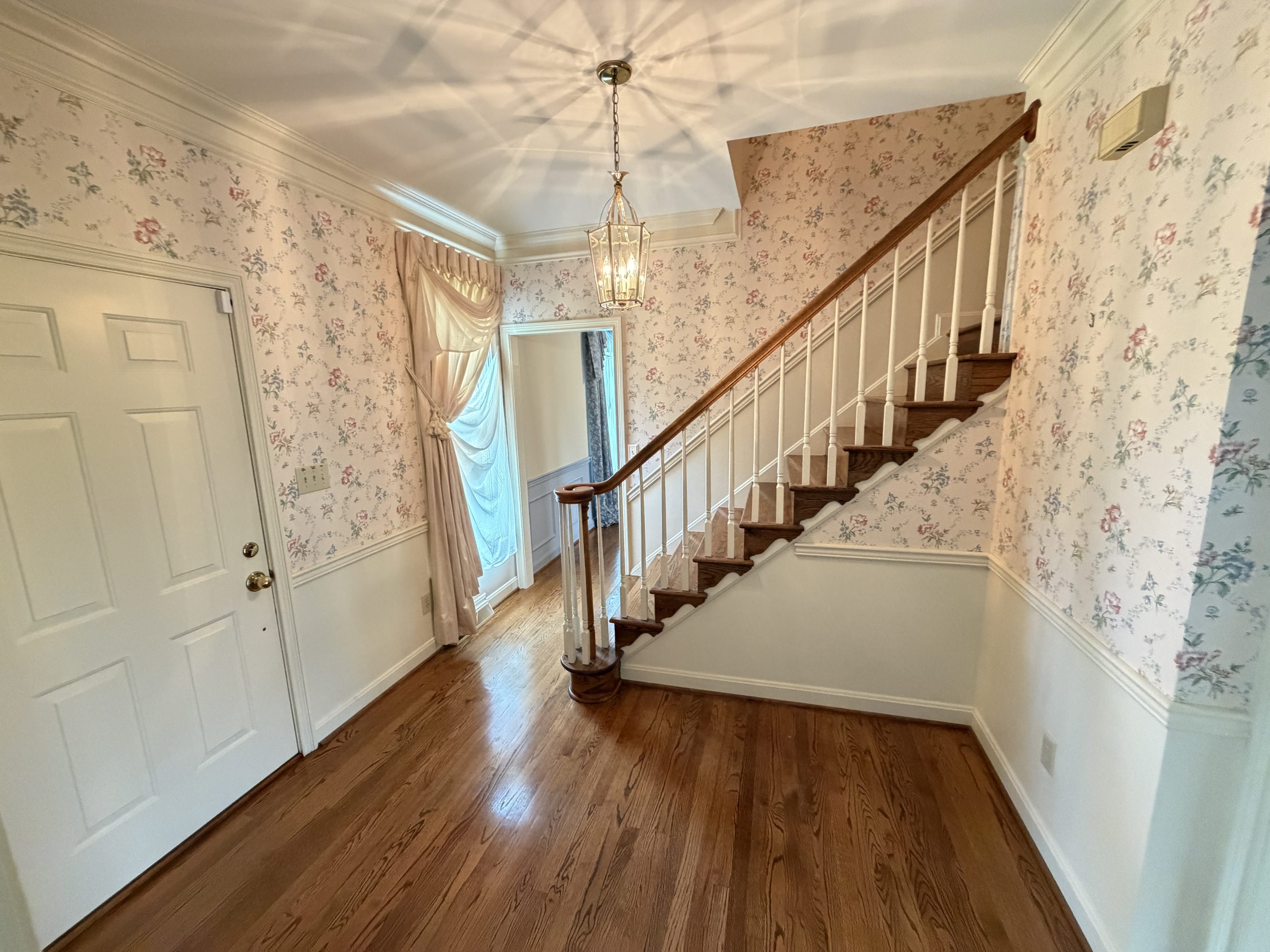 Entry hall with floral wallpaper, a wooden staircase railing, and a hanging lantern light.