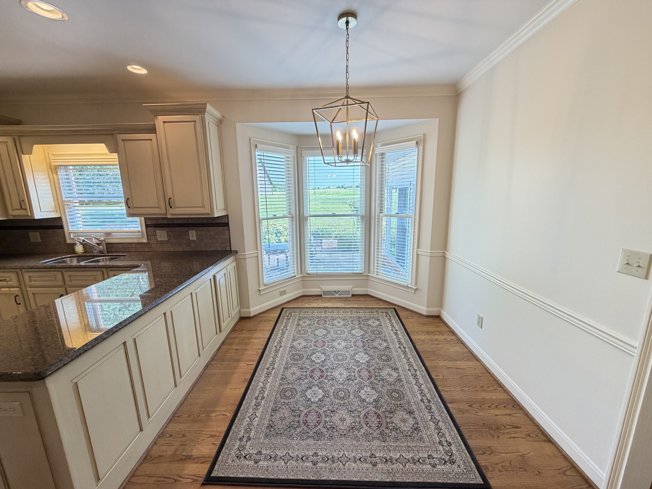 Bright kitchen with white cabinets, granite countertops, and a geometric pendant light over a patterned rug runner.