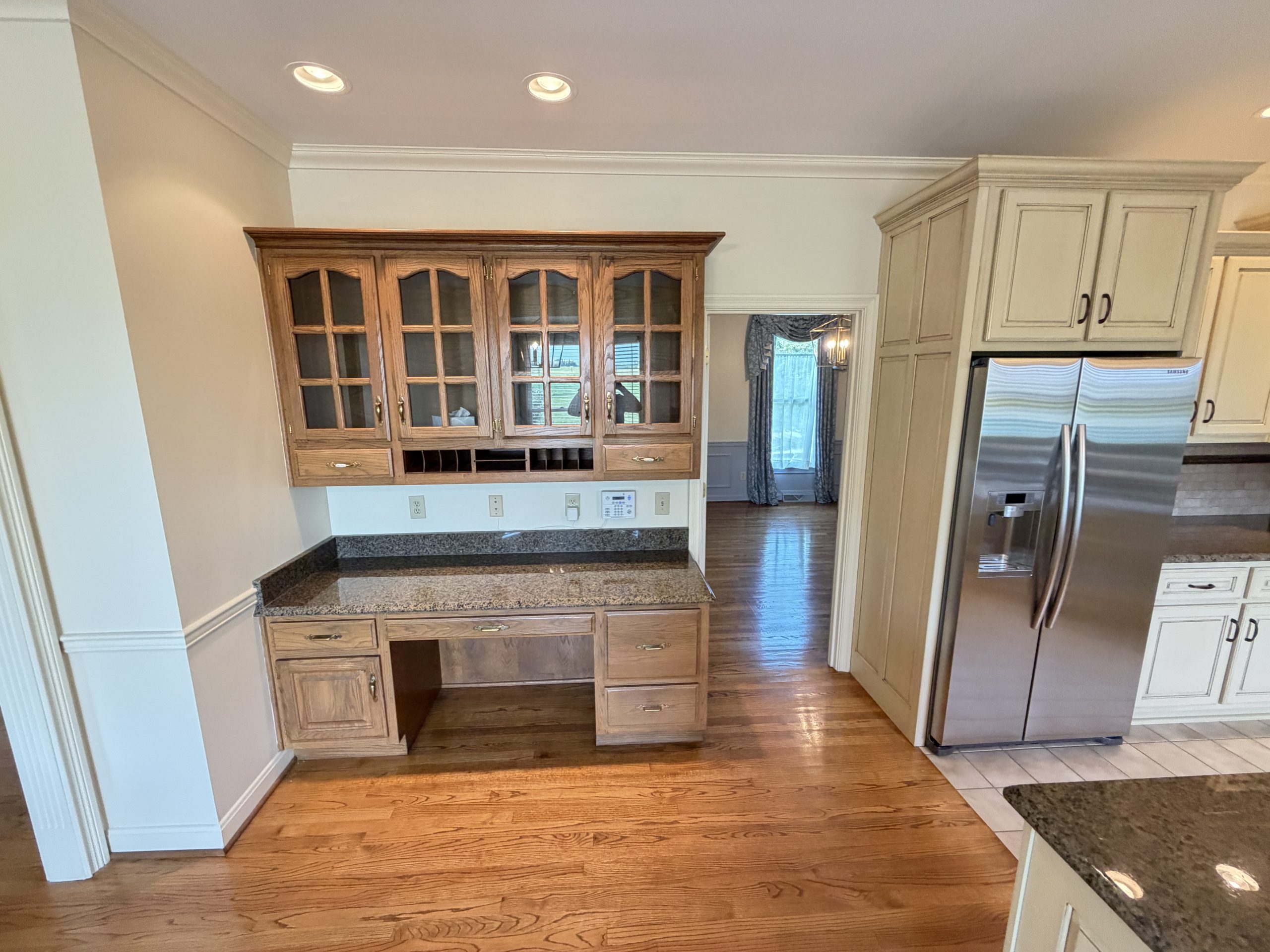 Kitchen with wooden glass-front cabinets, granite countertops, and a stainless steel side-by-side refrigerator to the right.