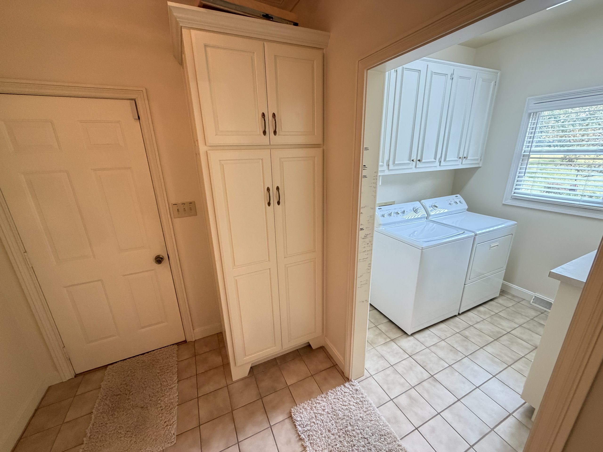 Laundry area with white cabinetry, a washer and dryer side by side under a window with blinds, and tiled floor.