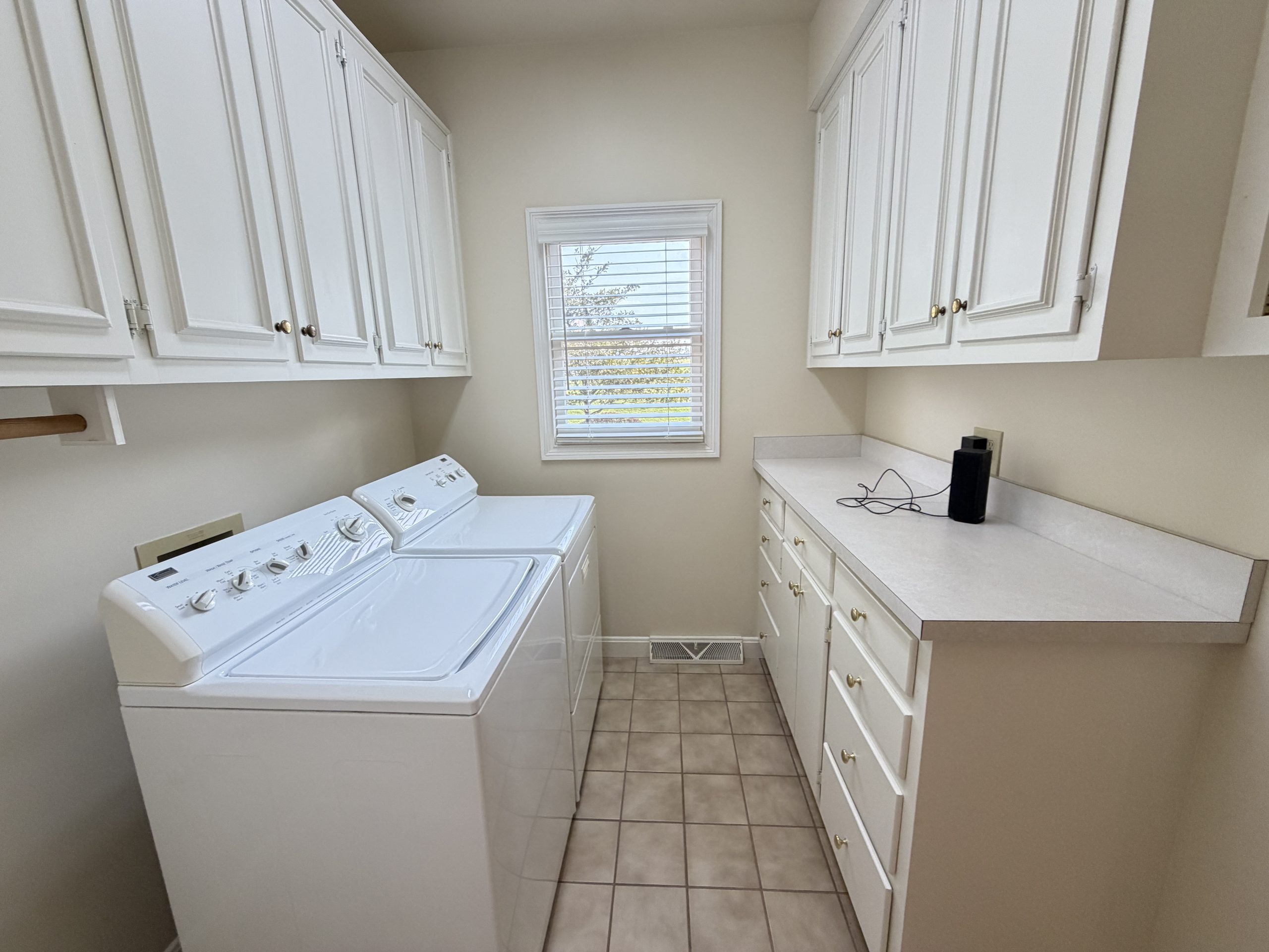 Laundry room with white cabinets overhead, a front-loading washer and dryer, and a window with blinds at the far wall.