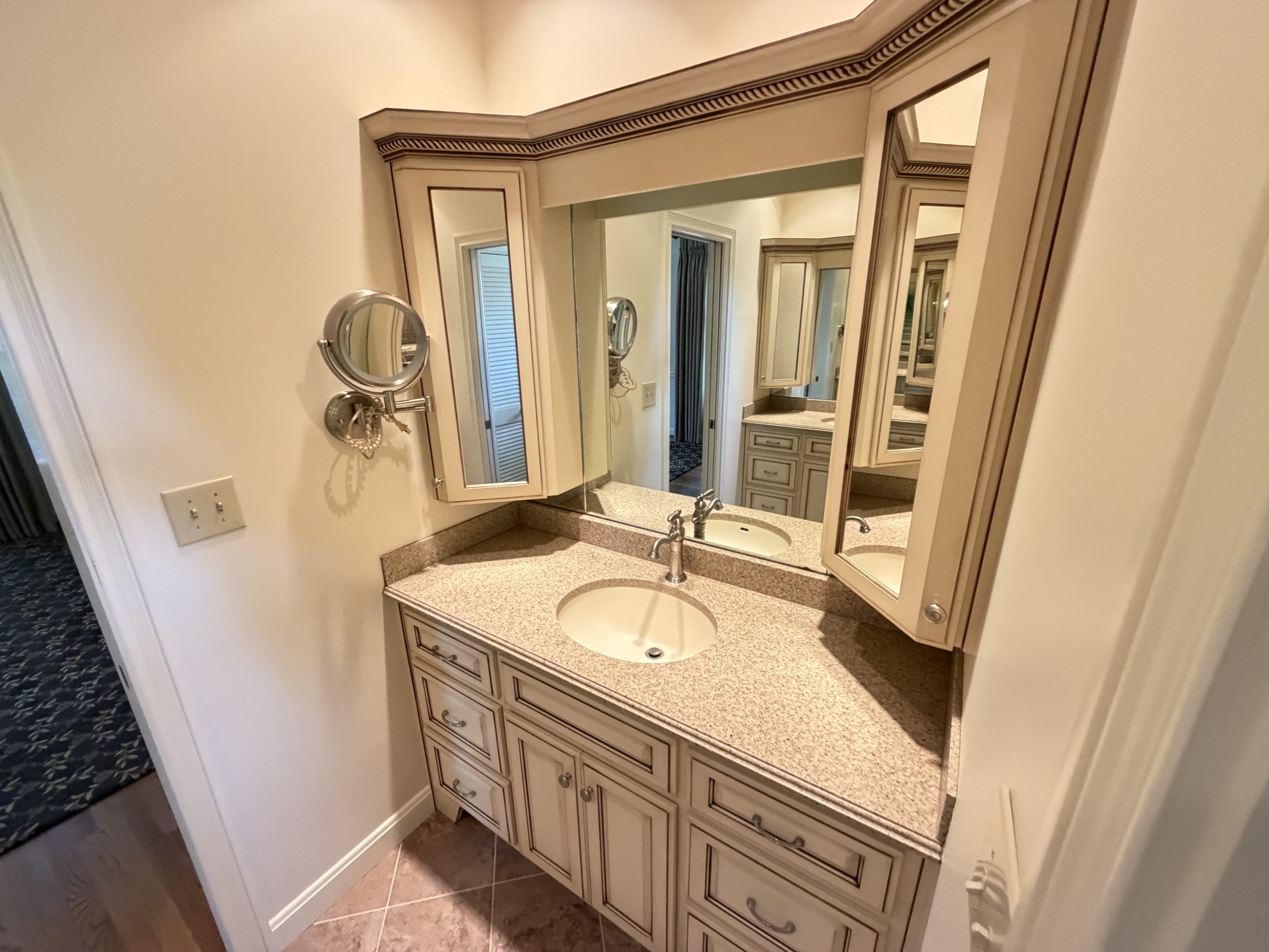Beige bathroom vanity with speckled countertop, two sinks, and mirrored medicine cabinets.
