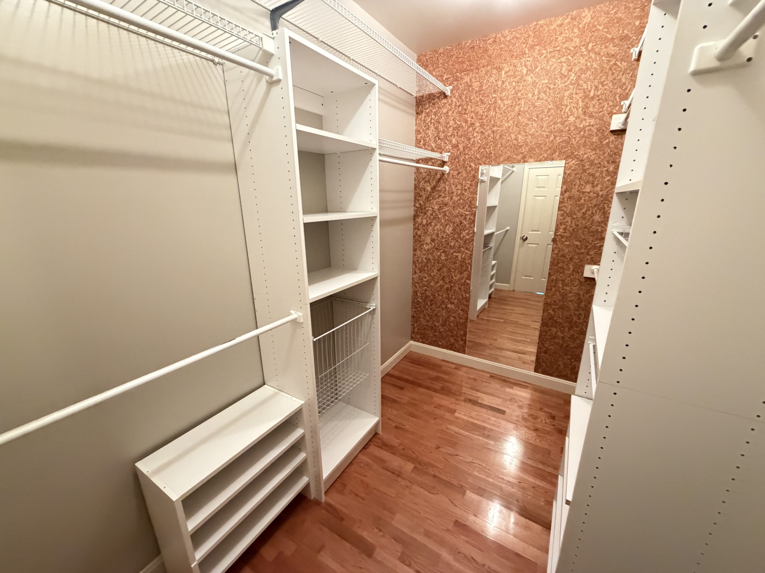 Walk-in closet with white shelving units, hanging rods, and a brown textured accent wall. Empty storage space ready for use.